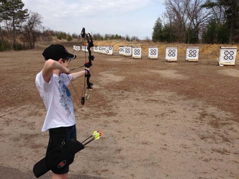 Young archer drawing a compound bow toward targets on an outdoor range