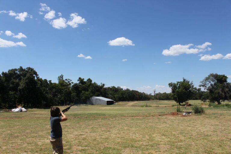 Shooter breaking clay targets on an open trap field under blue sky